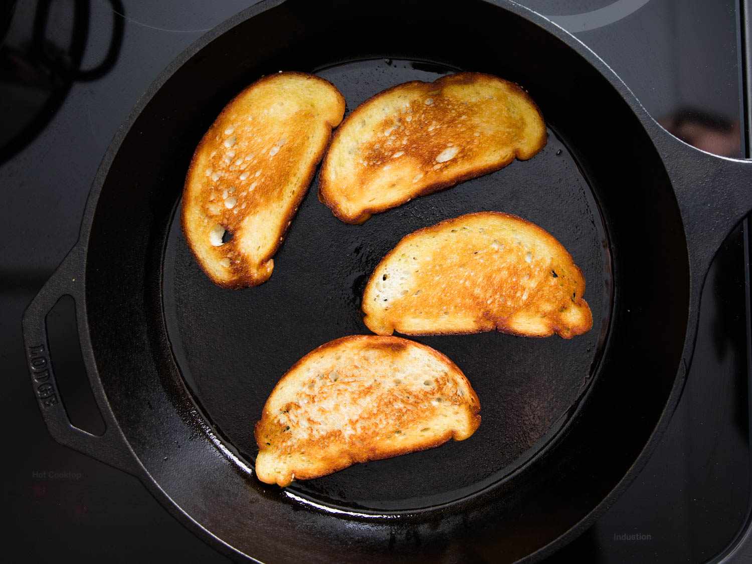 Overhead view of sliced country white bread toasting in a cast iron skillet.
