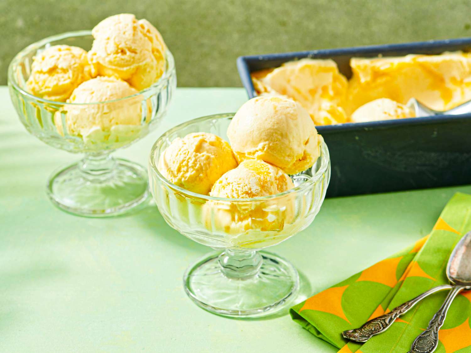 Scoops of mango ice cream in glass bowls with an ice cream tub in the background