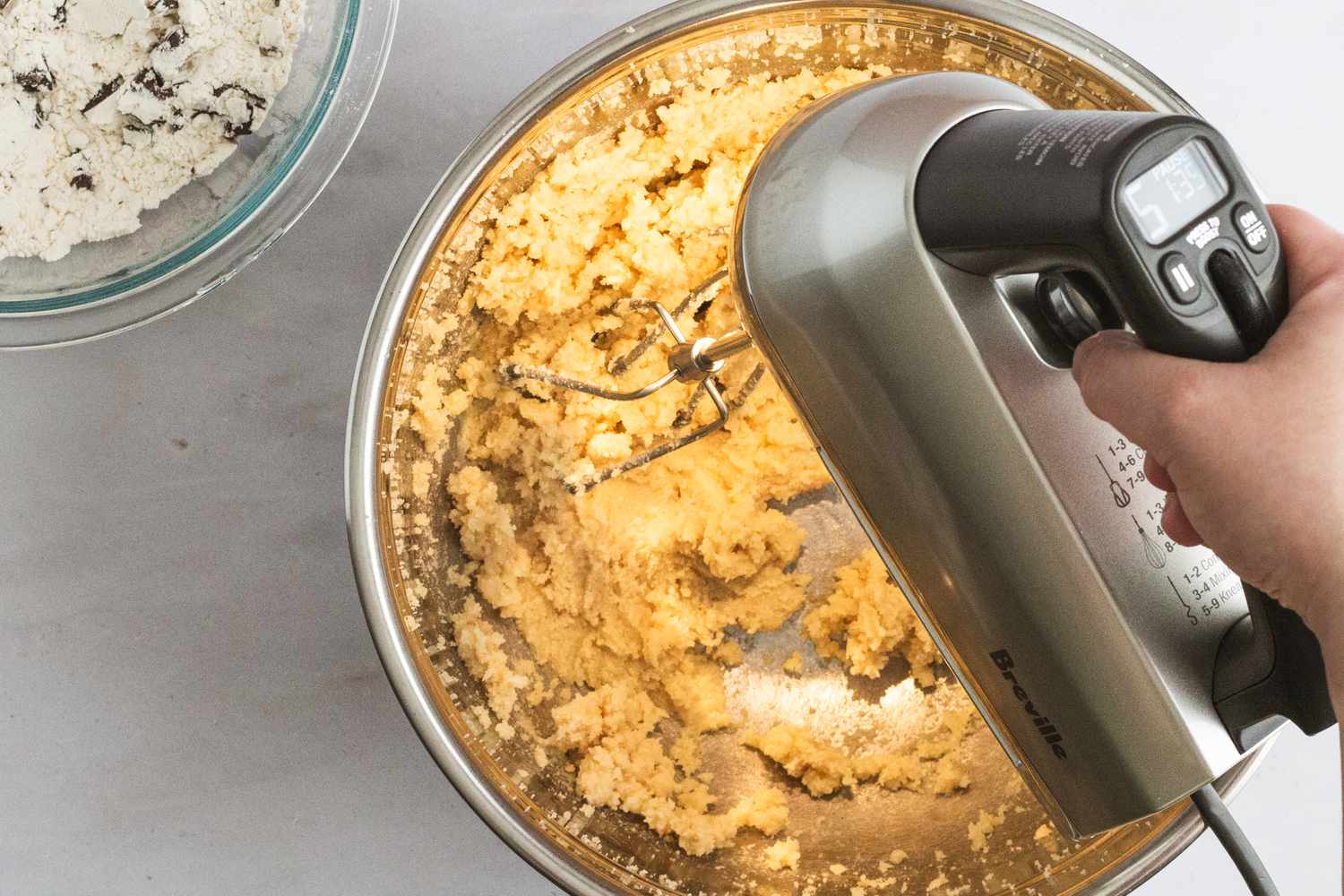A person using a Breville hand mixer to mix cookie dough.