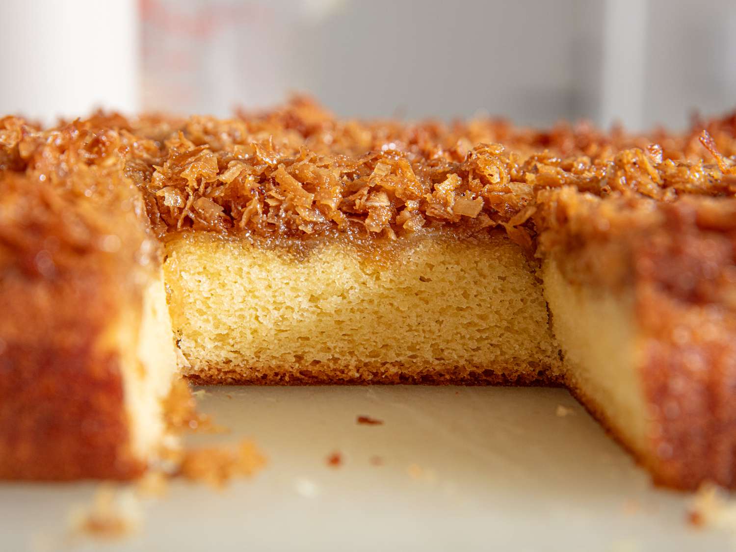 A slice cut out of a rectangular piece of Lazy Daisy cake, exposing its moist interior texture and caramelized coconut topping