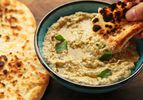 Dipping pita bread into baba ganoush in a small bowl, drizzled with olive oil.