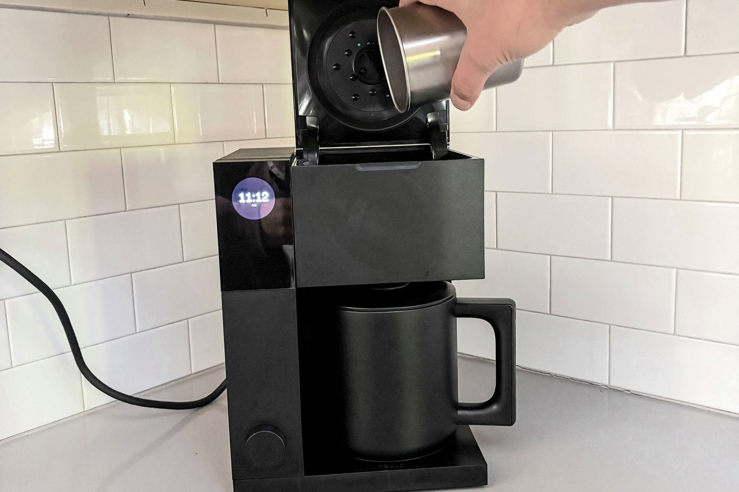 A person adding ground coffee beans to the Fellow Aiden.