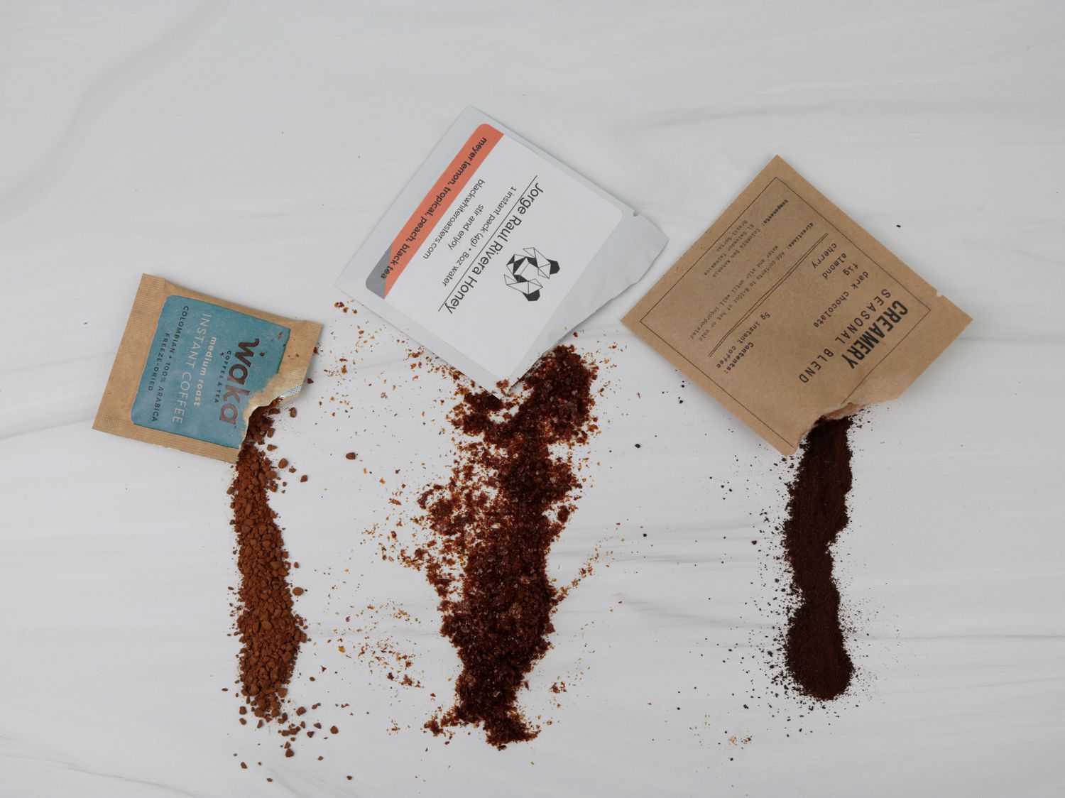 three different instant coffee packets with instant powder spilling out of them