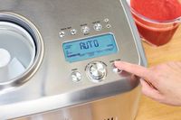 A finger pressing a button on the Breville Smart Scoop Ice Cream Compressor