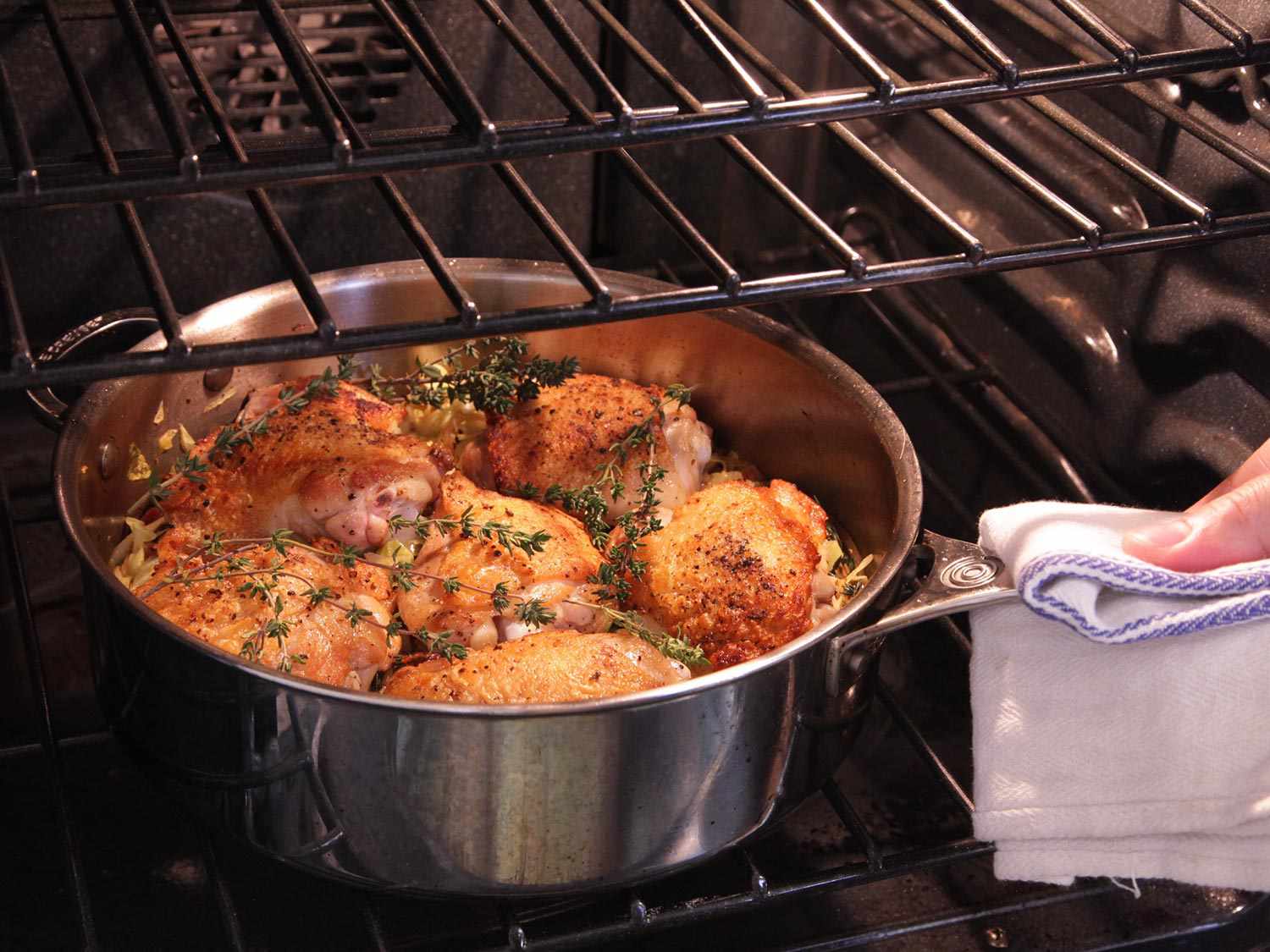 Placing a pan of chicken thighs with cabbage and bacon in the oven.