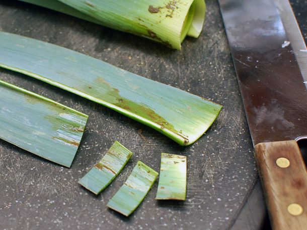 Stalks of leek greens on a black surface. Half of one stalk has been cut into thin segments. 