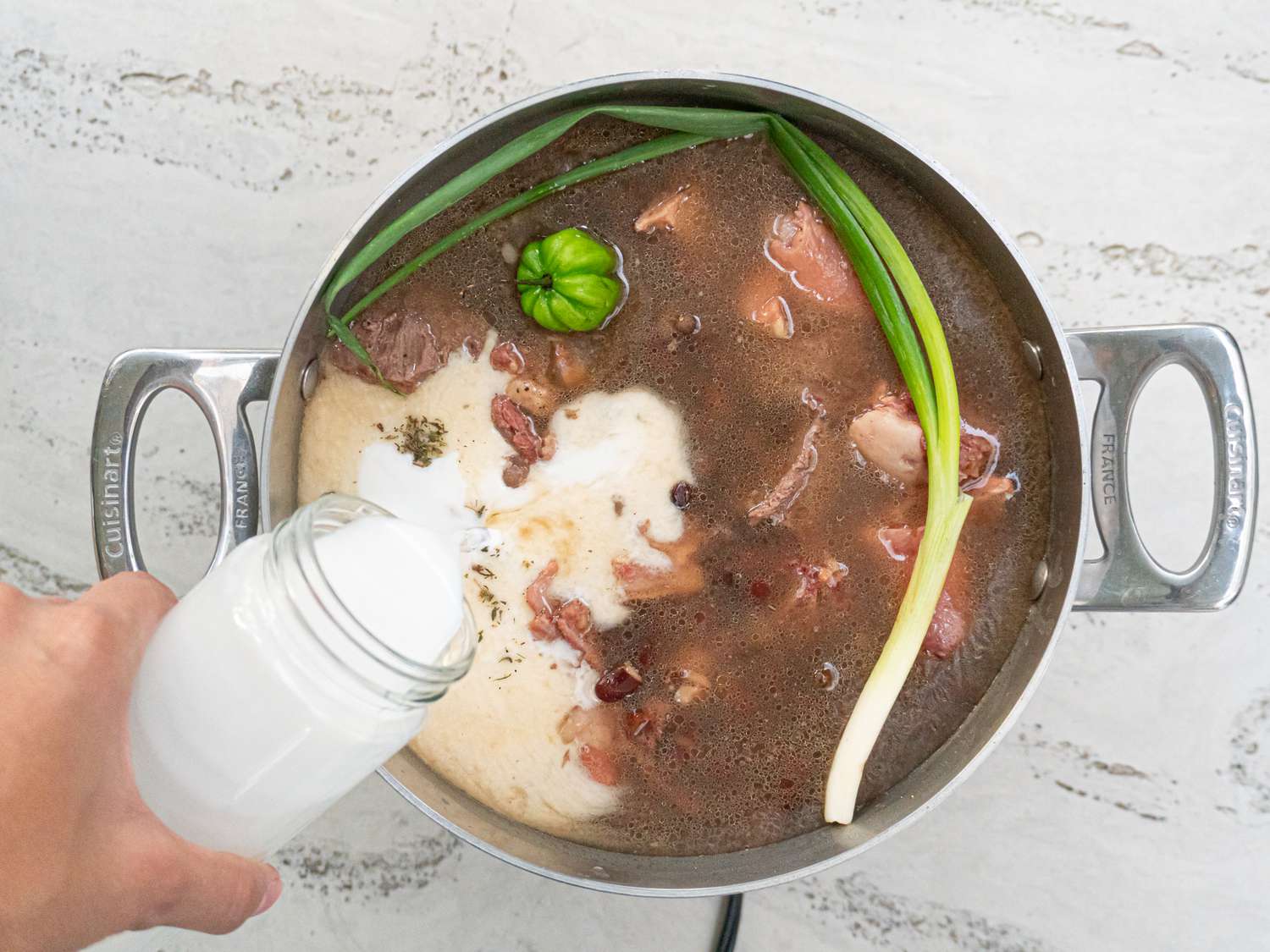 Overhead view of adding coconut milk into stew peas