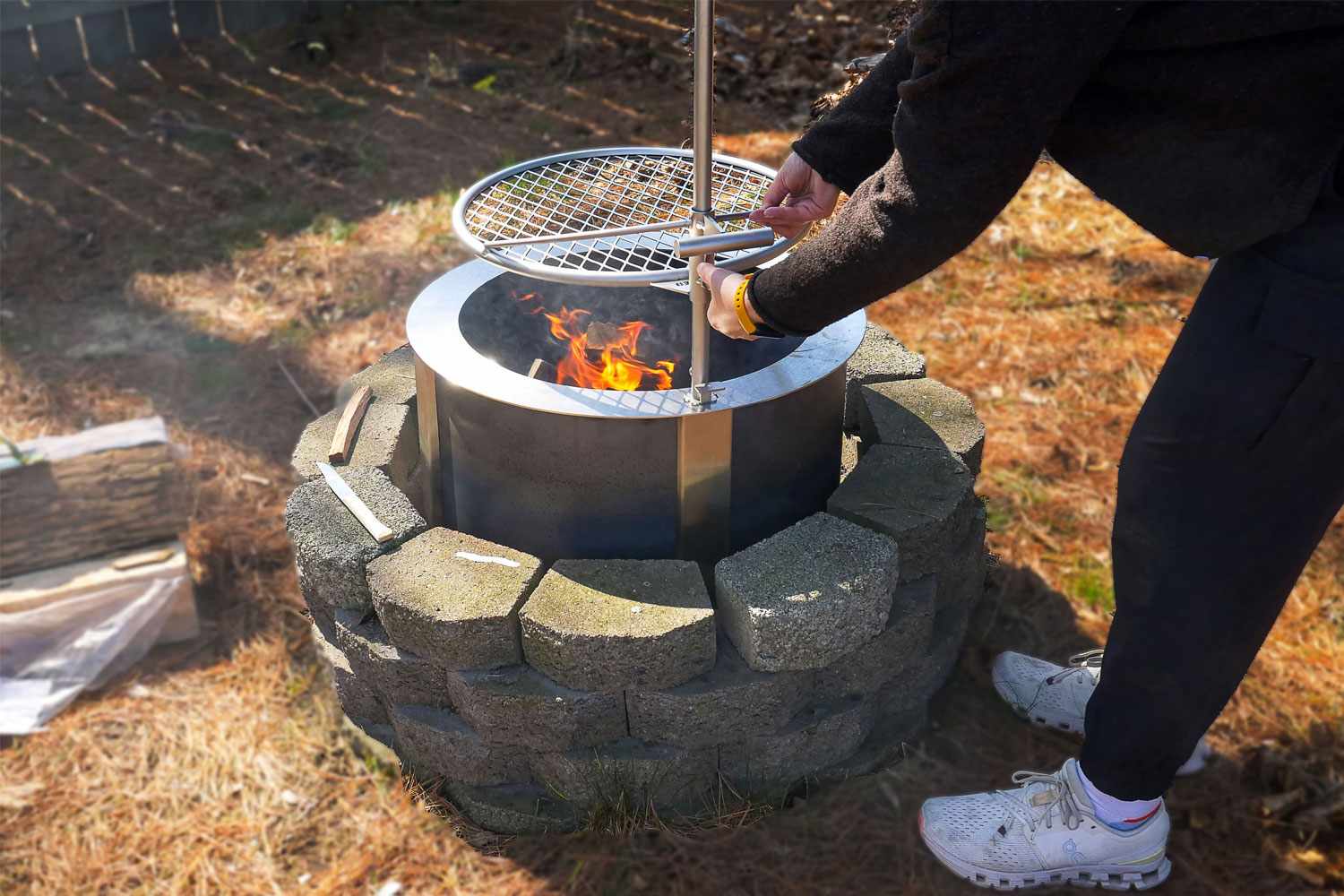 A person adjusting the grill over a fire pit with a burning flame inside