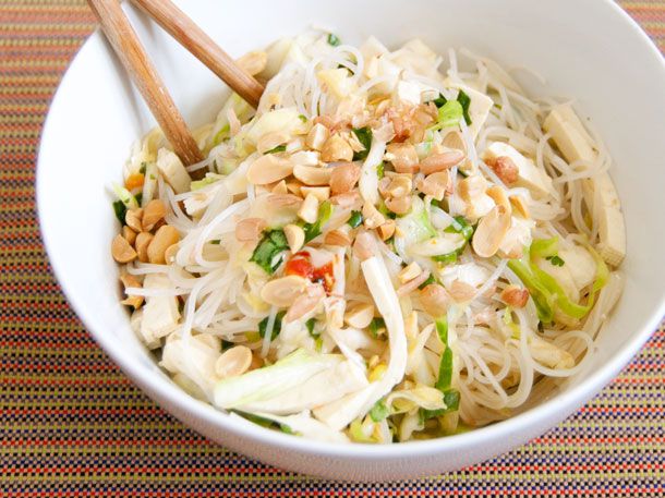 A white bowl of spicy rice noodle salad with sliced cabbage, peanuts, and tofu 