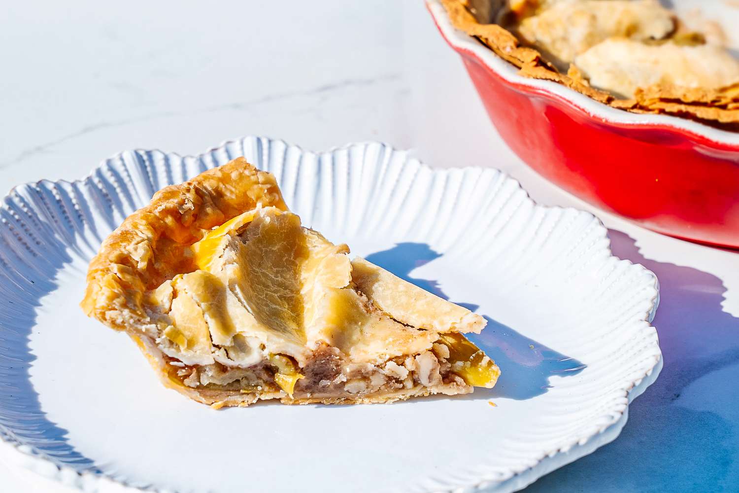 A slice of pie on a white plate with a red Emile Henry Modern Classics Pie Dish in the background