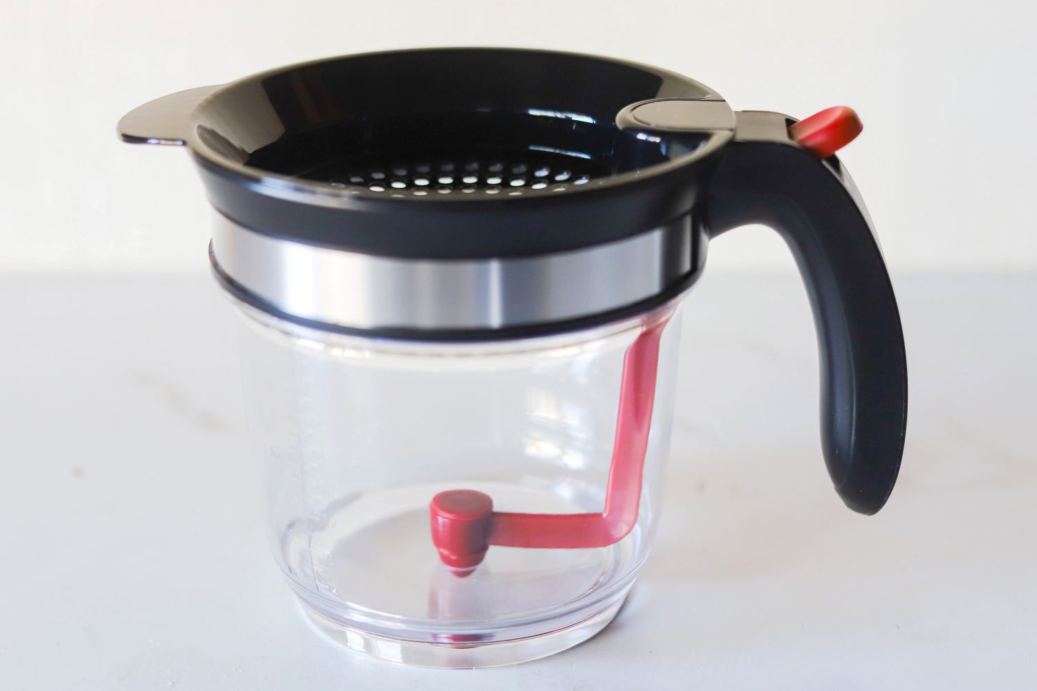 A transparent container with a black lid handle and a red lever mechanism inside