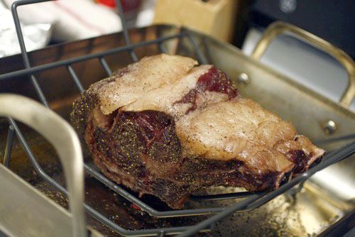 Cooked prime rib roast on a rack in a roasting pan with un-rendered fat cap.