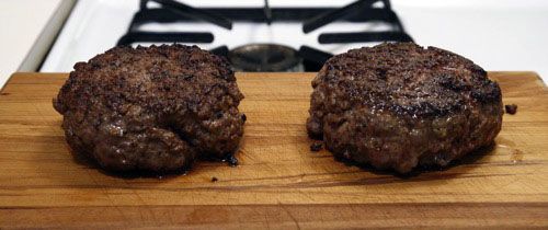 Two burgers on a wood cutting board showing their browned exteriors.