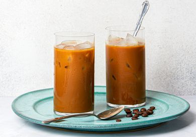 Two glasses of Vietnamese iced coffee on a blue plate with coffee beans.