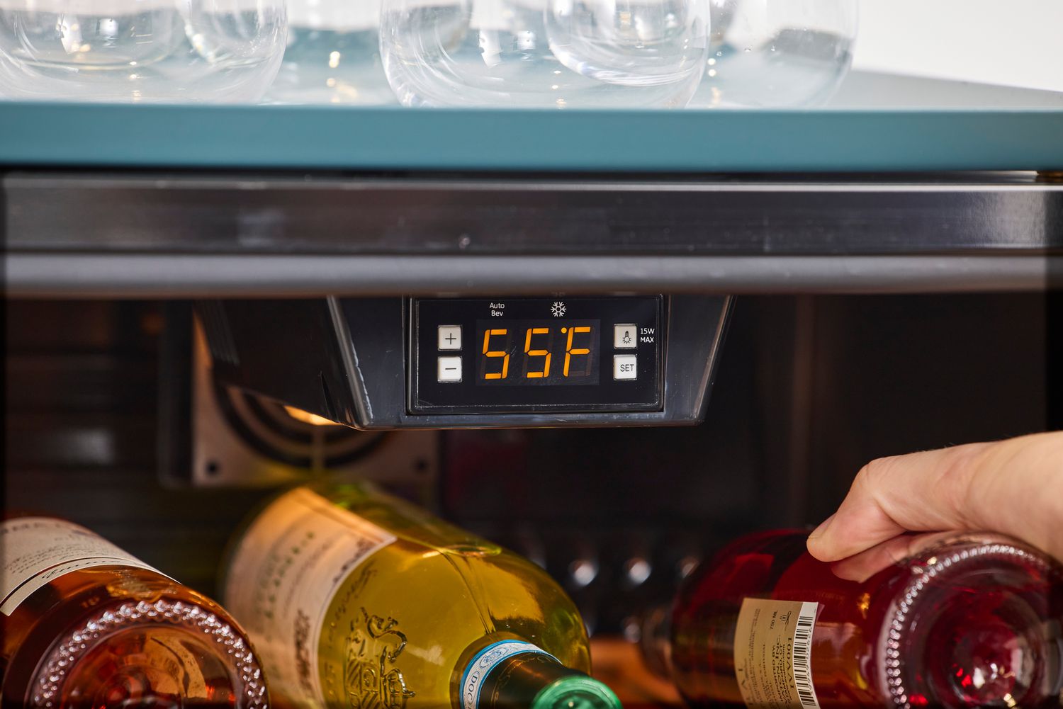 A hand placing a wine bottle in a refrigerator set to 55°F