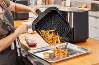 A person emptying fries from the Instant Vortex Plus 6QT XL Air Fryer onto a baking sheet
