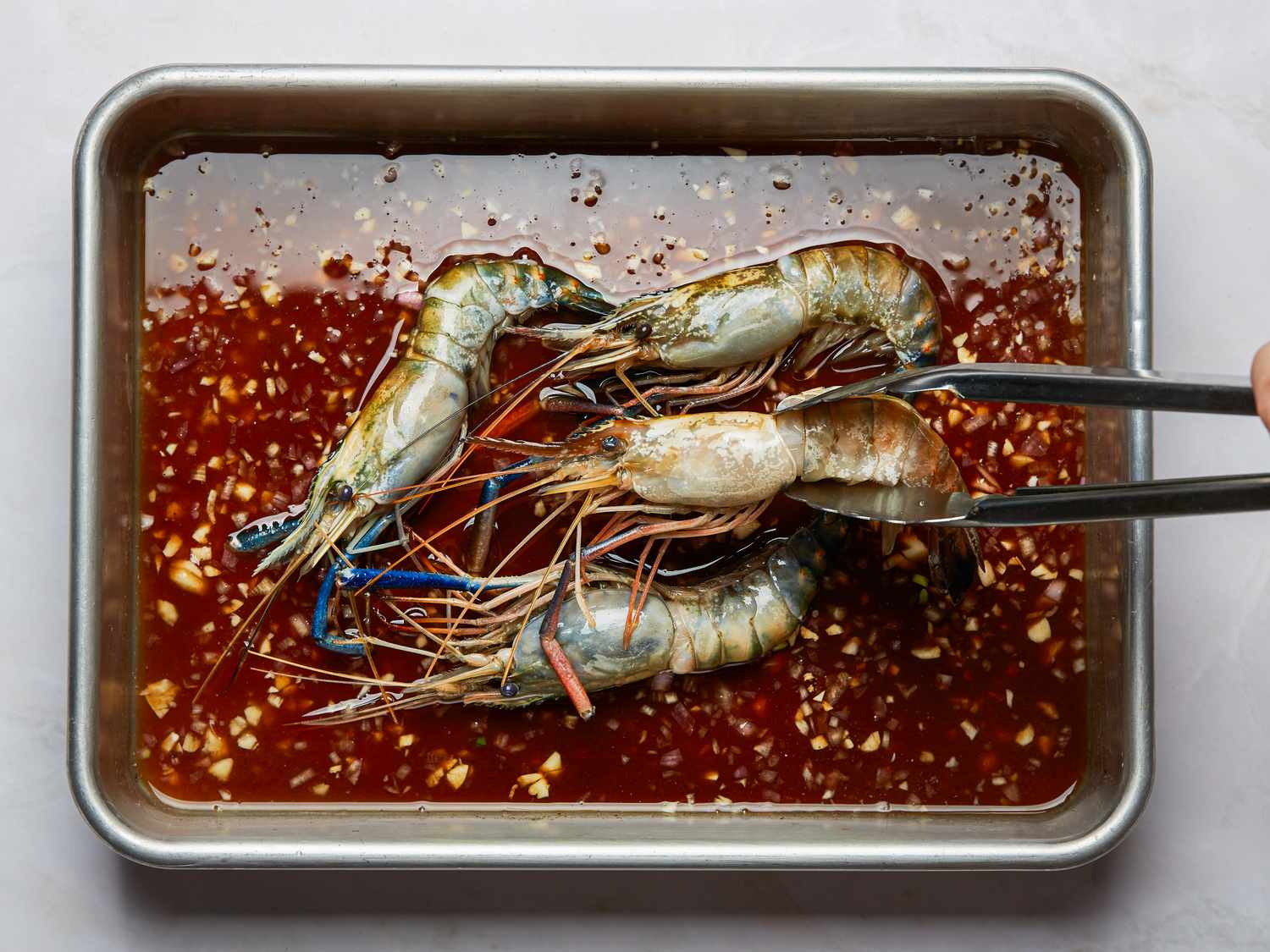 Tongs holding a marinated prawn other prawns in a marinade tray