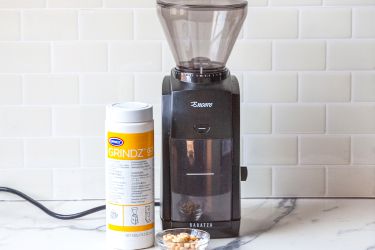 A coffee grinder and a bottle of coffee grinder cleaner on a wooden countertop.