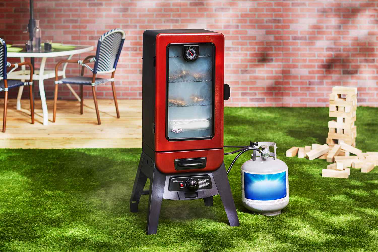 The Pit Boss propane smoker sits in a backyard, with a large Jenga set in the background..