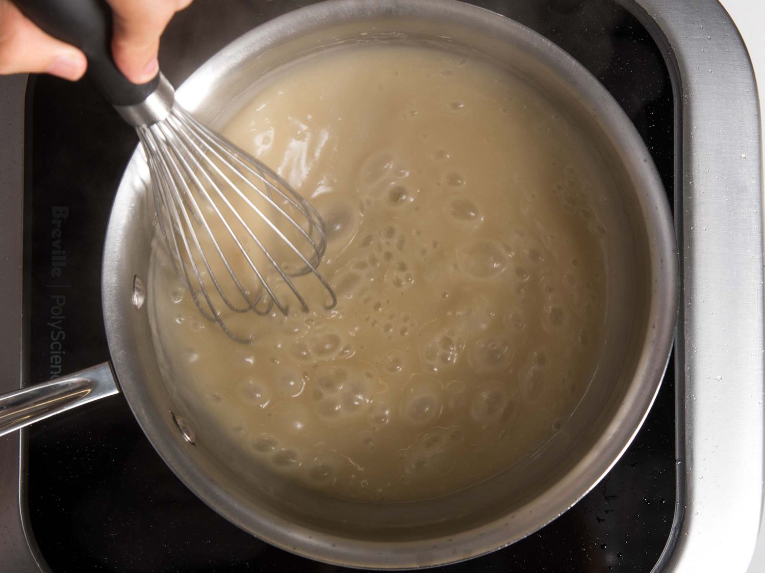 Simmering and whisking thick gravy in a saucepan over an induction burner.