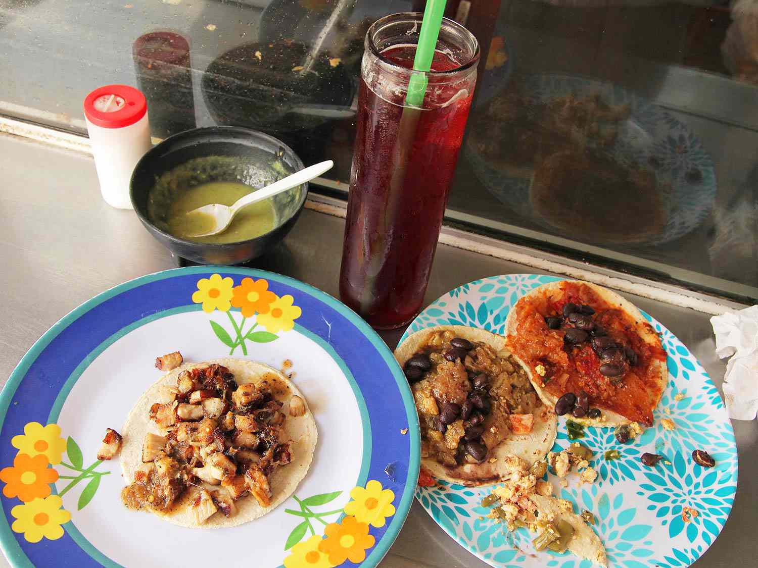 Tacos from Wayan'e, served on colorful mismatched plates with a tall glass of agua fresca de jamaica.