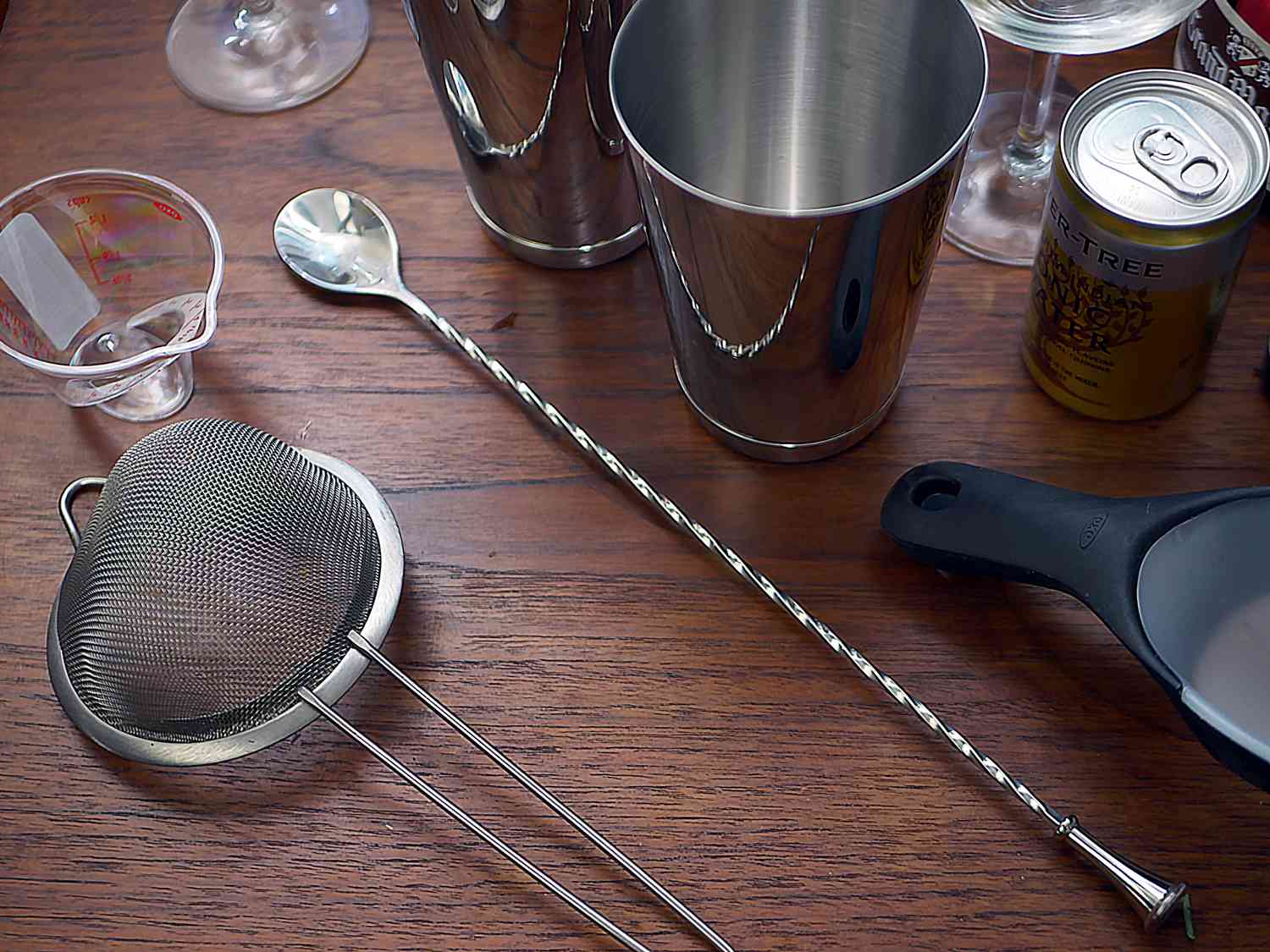 an overhead shot of a bar spoon, strainer, small measuring cup, and Boston shakers