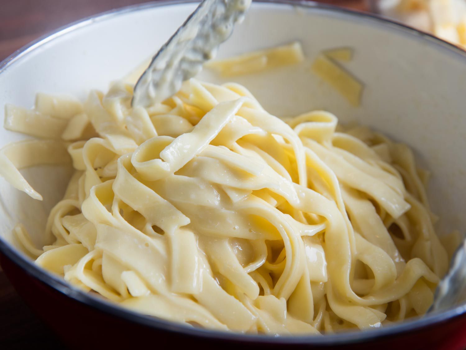 Tossing together hot pasta, butter, and grate Parmigiano-Reggiano cheese with tongs.