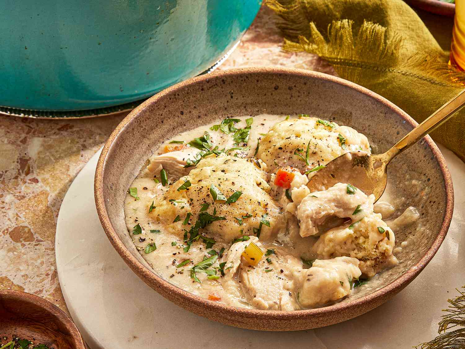 Close up of a bowl of Chicken Dumpling soup in rustic stoneware bowl, with a dark green napkin to the side, and a gold spoon in the soup