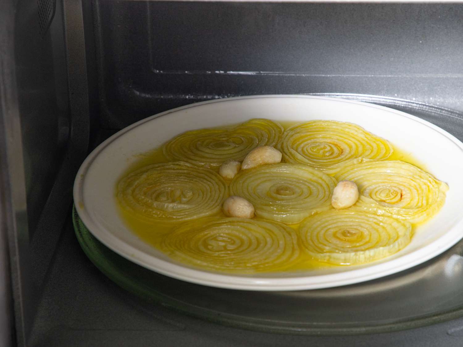 A microwave oven with a plate of sliced onions and cloves inside