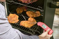 A person checks the temperature of chicken cooked in the Cuisinart COS-244 Vertical 36-inch Propane Smoker