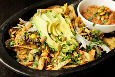 Chilaquiles with pepitas, charred corn, and black beans are served in a black earthenware platter.