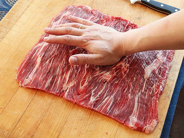 Hand pressing down on large square of butterflied flank steak