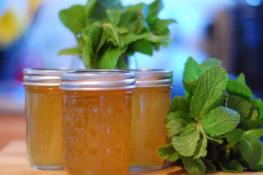 Profile view of several half-pint jars of mint jelly, flanked by bunches of fresh mint.
