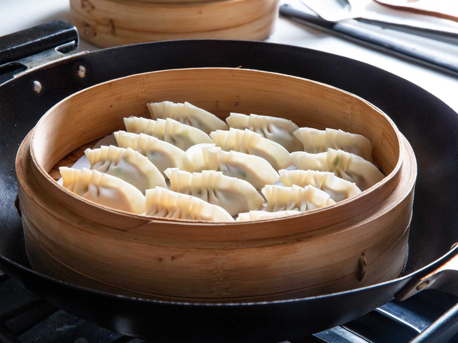 Side view of pork and scallion dumplings in a bamboo steamer set in a wok.