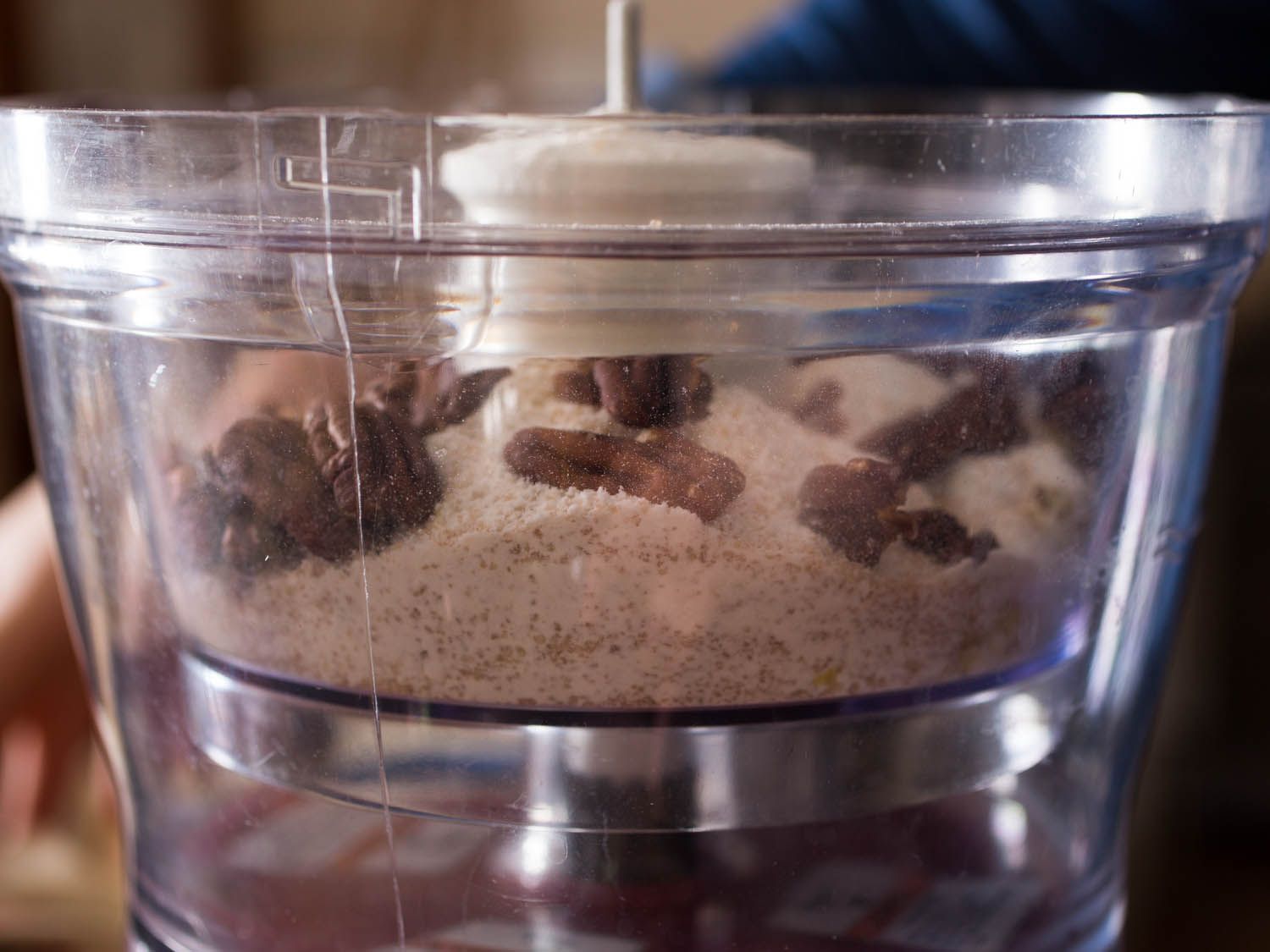 Close-up side view of dry mix for crumb topping in the bowl of a food processor, with pecan halves on top.