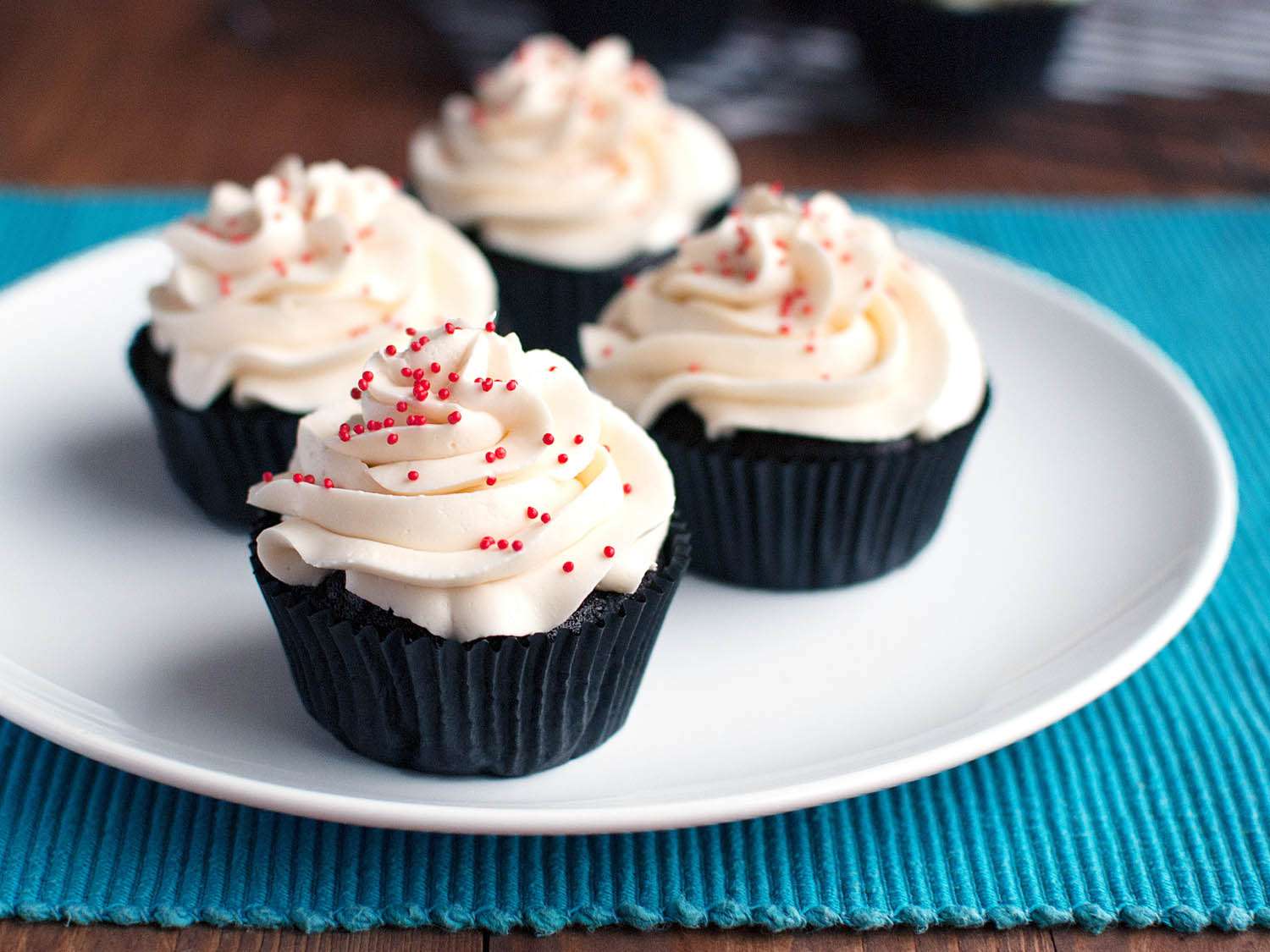 Four buttercream cupcakes resting on a white plate.