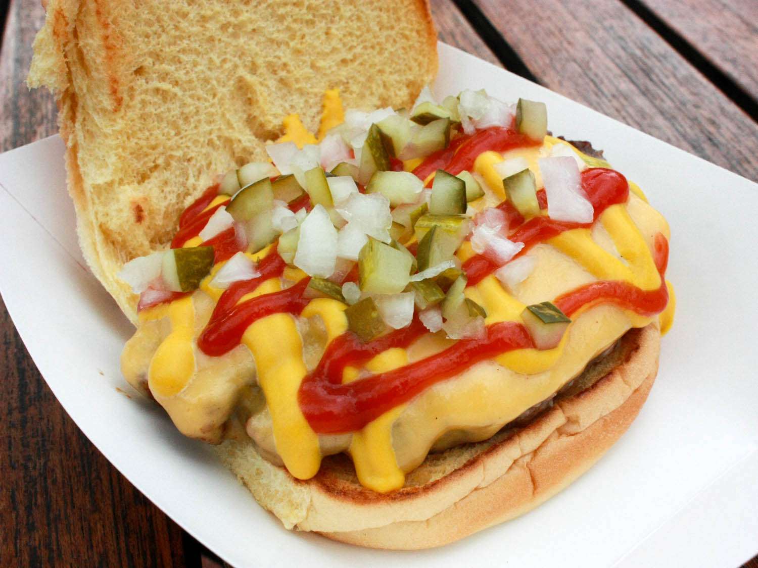 Cheeseburger with ketchup, mustard, pickles, and onions with the top bun removed.