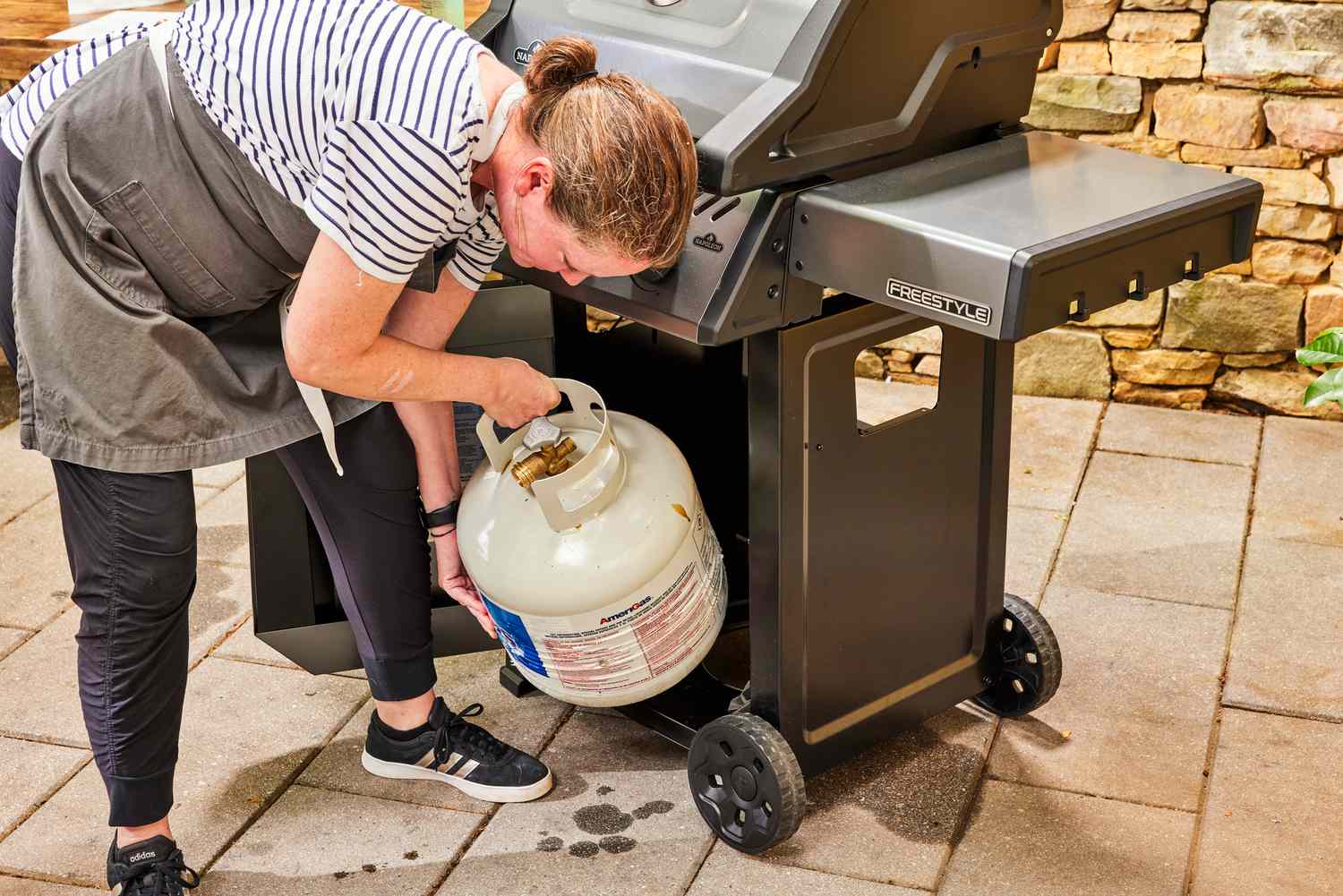 A person places a propane tank in the Napoleon Freestyle 365 Gas Grill