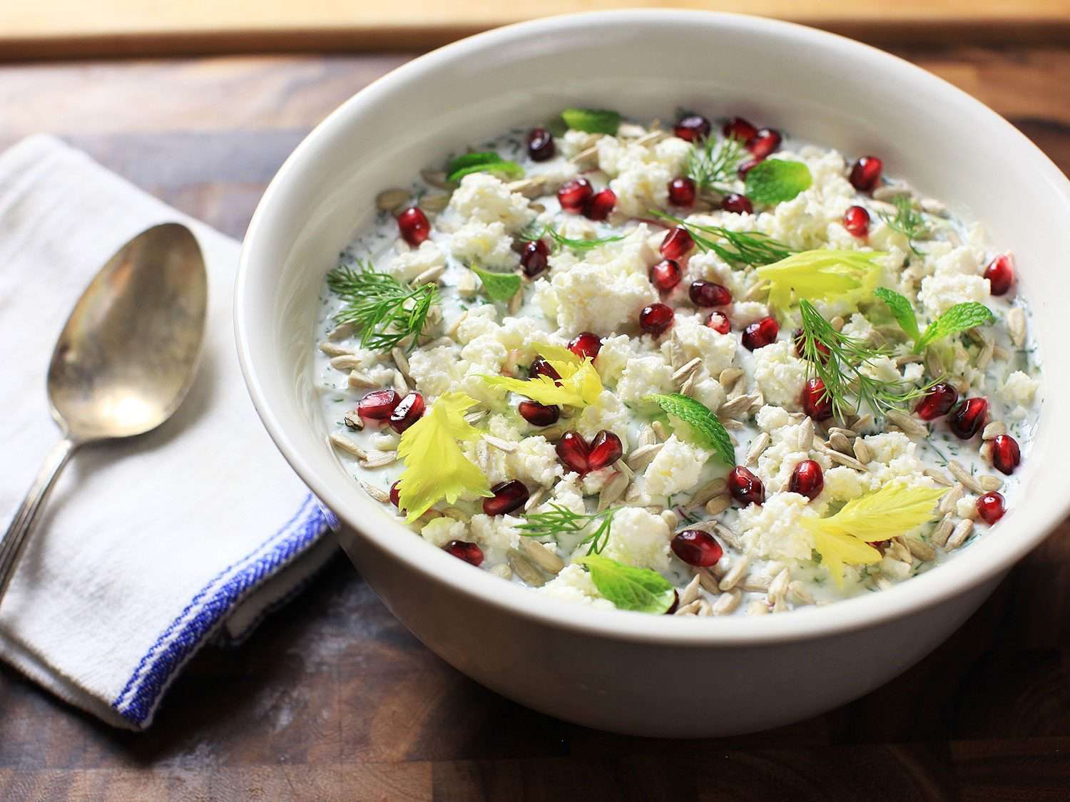 7-Layer Make-Ahead Salad With Chickpeas, Endive, and Yogurt Dressing garnished with pomegranate seeds and mint in a bowl.