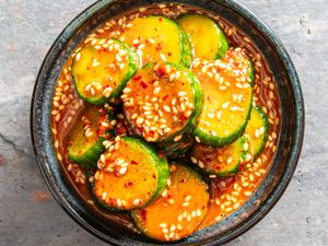 A bowl of marinated cucumber slices topped with sesame seeds and red chili flakes