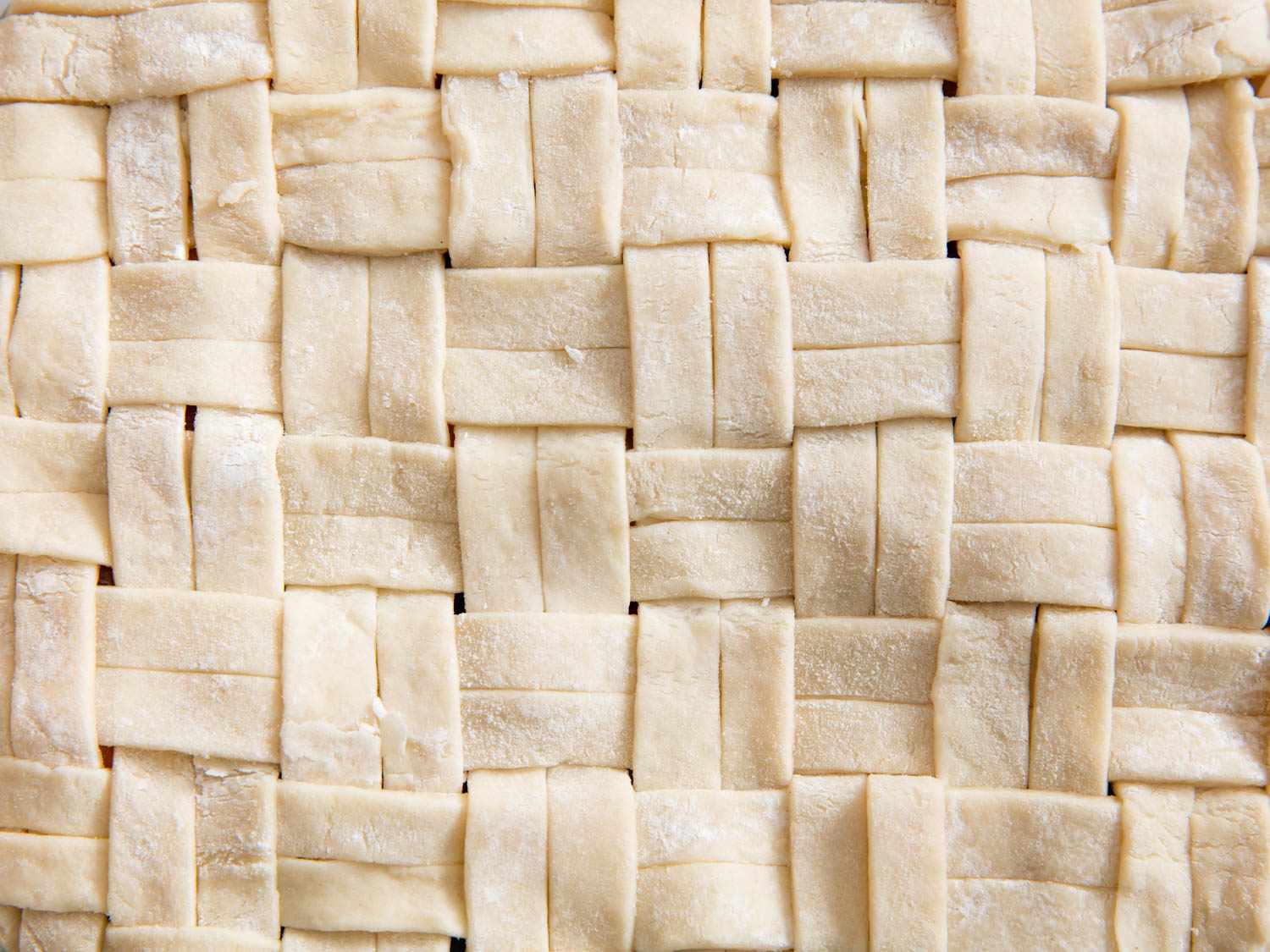 Close-up of unbaked pie dough strips laid out in a basketweave-style pattern for the pie's top crust. 