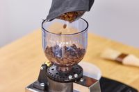 Coffee beans are poured into the Lelit Fred Tempo Burr Grinder
