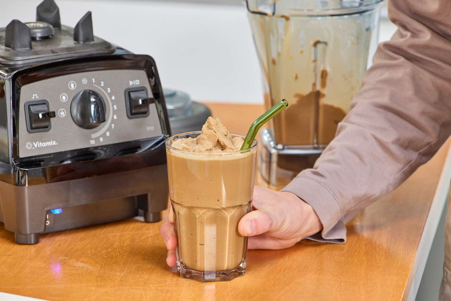 A hand holding a smoothie next to the Vitamix Propel 510
