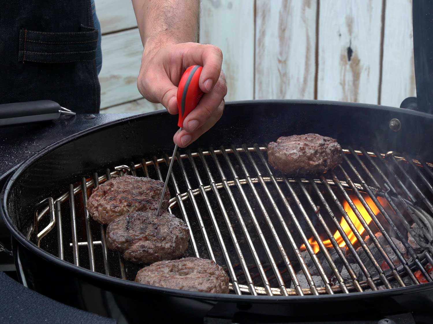 Burgers cooking on a gill and having their temperature checked with a thermometer 