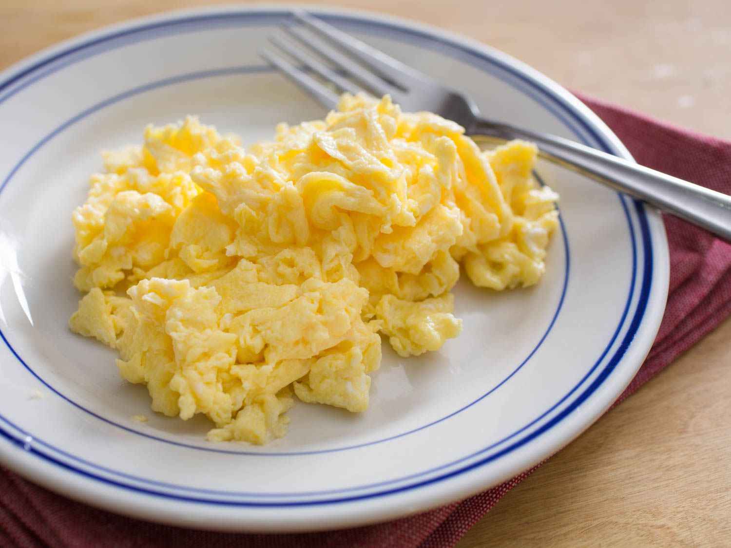 A white and blue plate with a pile of fluffy scrambled eggs and a fork. 
