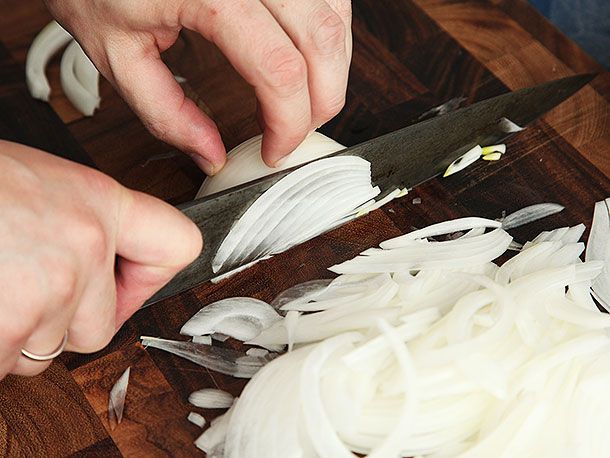 A knife slicing into an onion, with the blade of the knife now level with the cutting board.