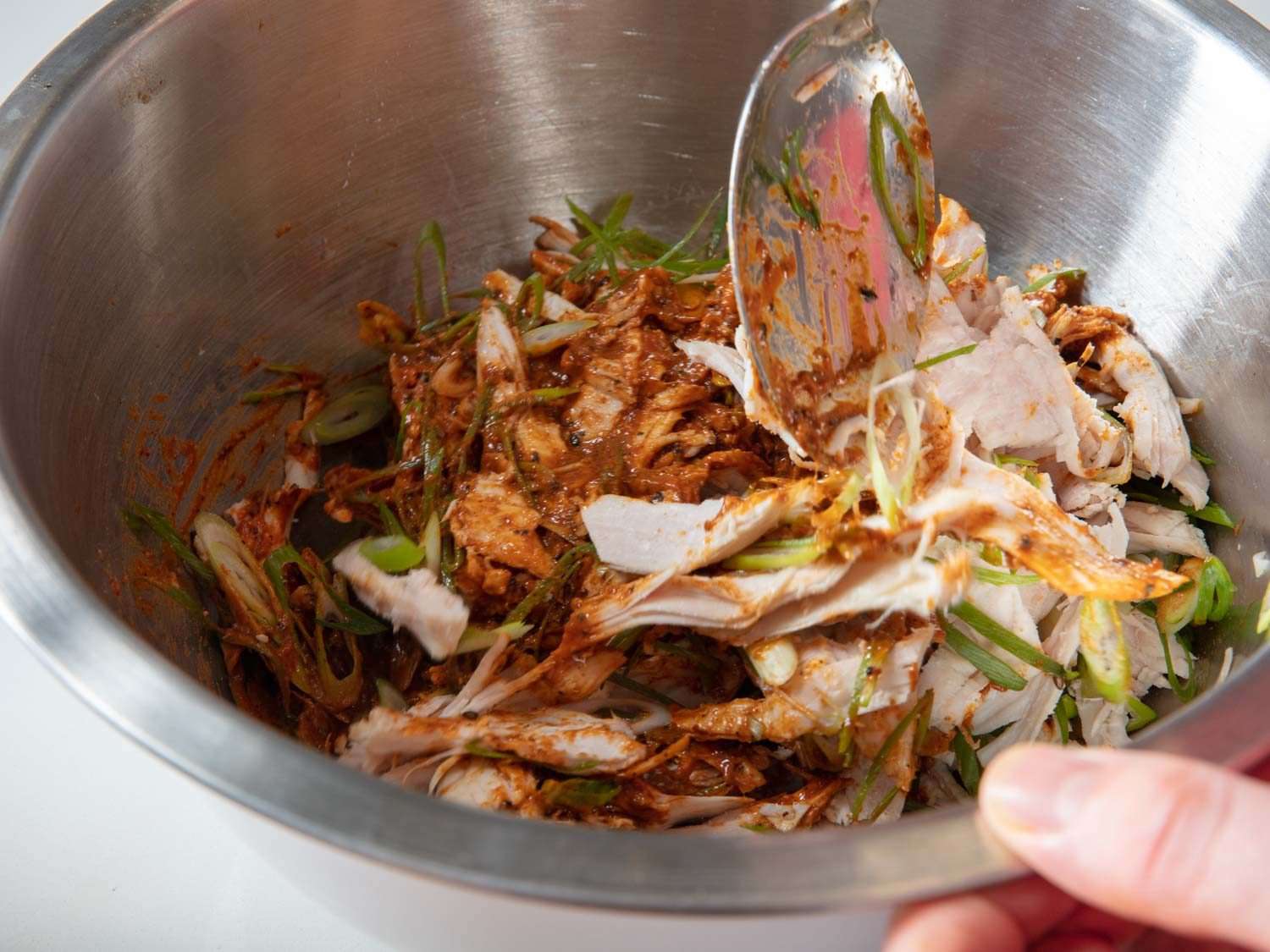 Mixing turkey together with dressing and sliced scallions in a mixing bowl.
