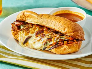 Vegetarian French dip sandwich with cheese and grilled vegetables on a platter, served with a cup of dipping broth