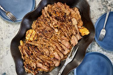 Overhead view of grilled butterflied leg of lamb in a serving platter surrounded by blue plates