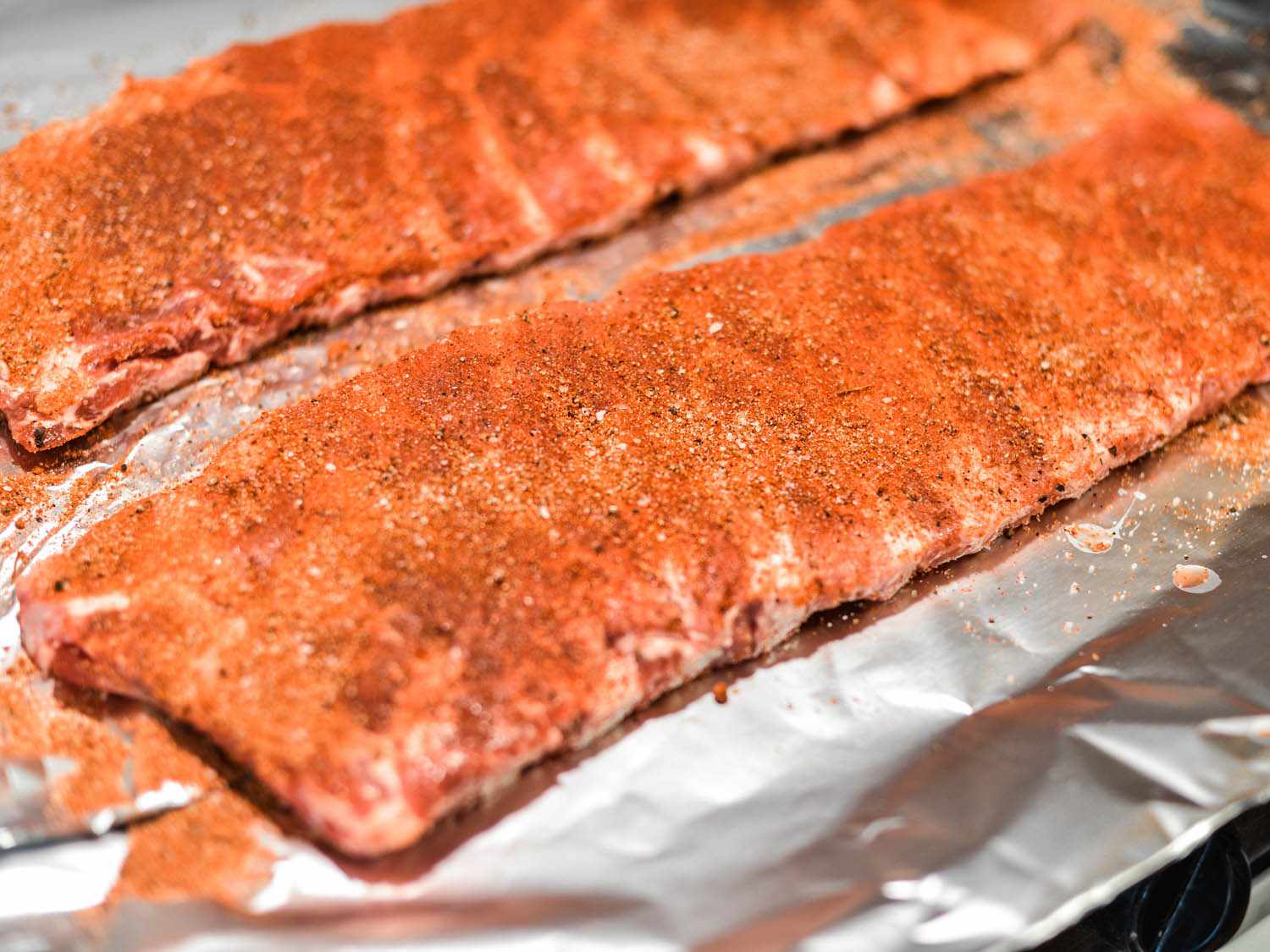 Two racks of pork ribs coated on aluminum foil coated with spice rub